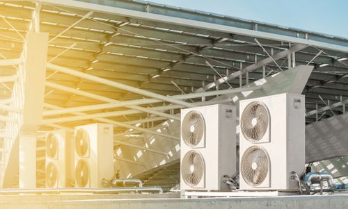 Klimaanlagenmodule in einer modernen Außeneinrichtung bei Sonnenlicht, unter einer Überdachung installiert.