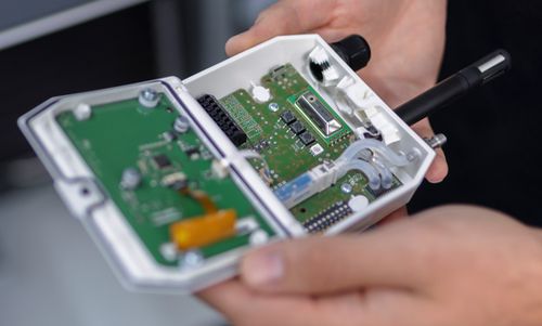Geöffnetes Feel-Gerät der FSM AG mit sichtbaren Leiterplatten und elektronischen Komponenten, gehalten von einer Person.