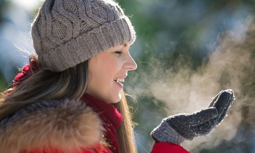 Frau in Winterkleidung, die in einer kalten Umgebung ihren Atem auf ihre behandschuhten Hände haucht.
